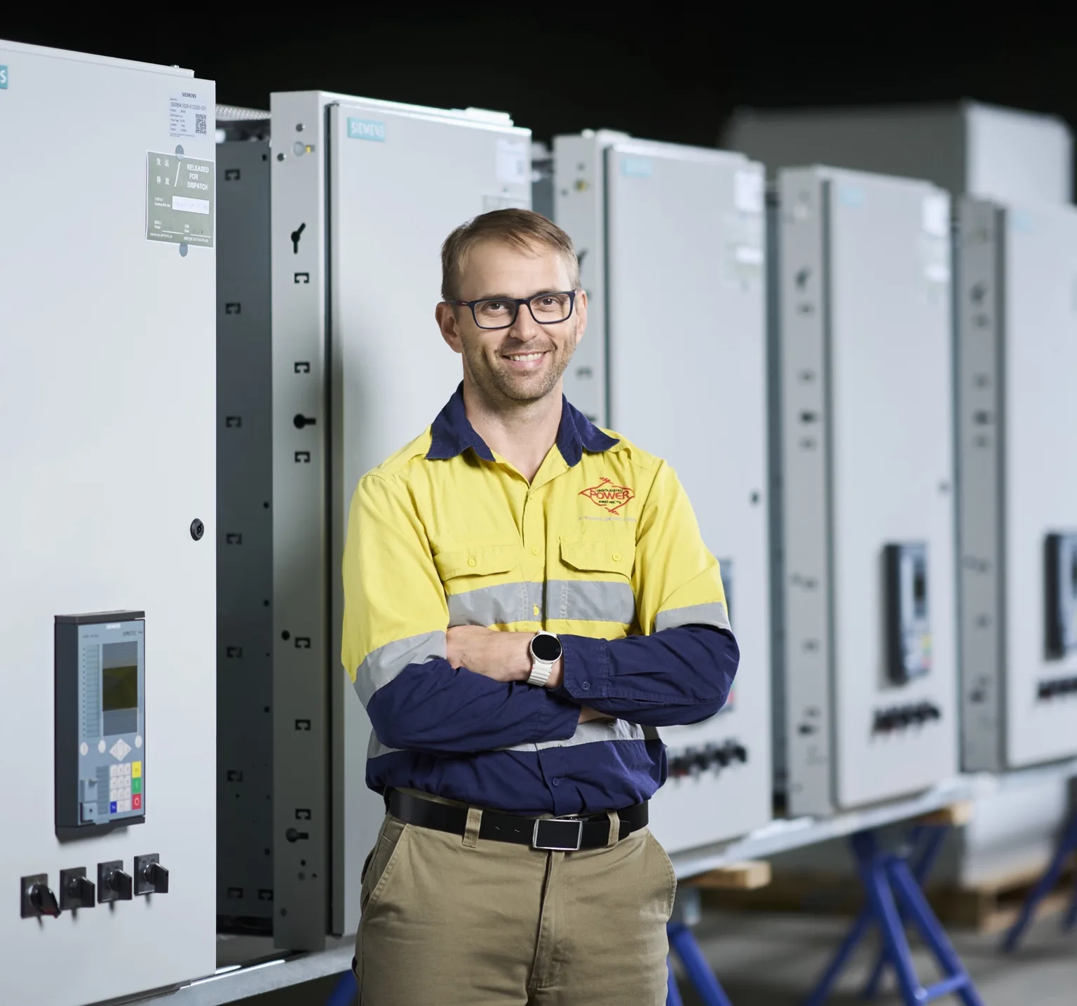 Engineer in high-vis workwear standing in front of electrical equipment.