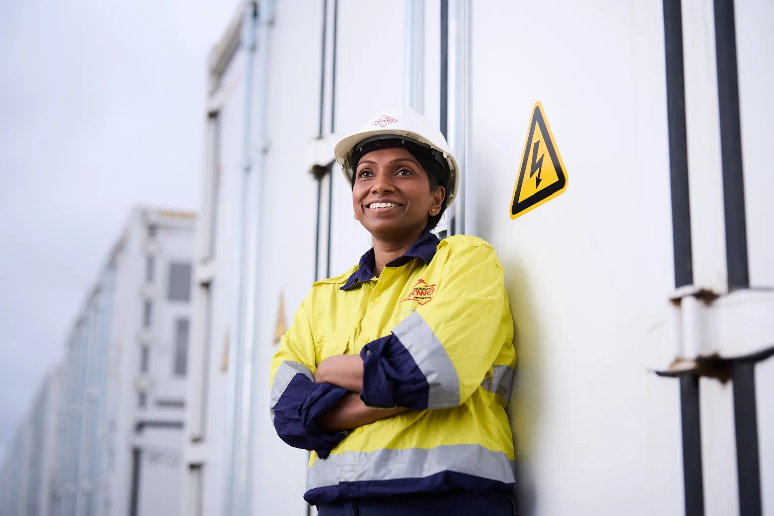 Engineer in high-vis workwear and hard hat standing beside electrical infrastructure.
