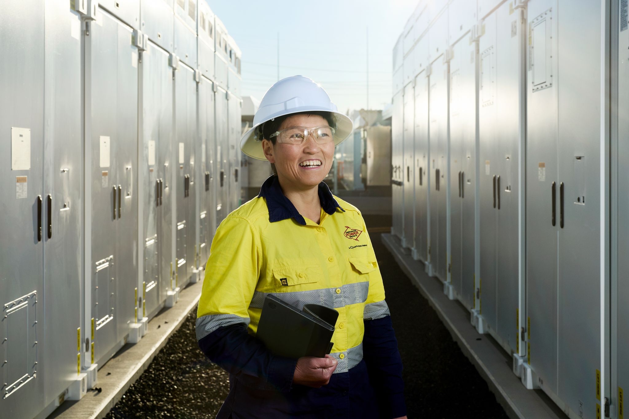 Engineer in high-vis workwear and hard hat standing between rows of electrical equipment.
